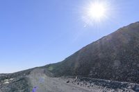 the sun shines brightly in the background as it casts a shadow on the side of a rock hill