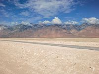 a desert field with a river in it with mountains behind it and clouds in the sky