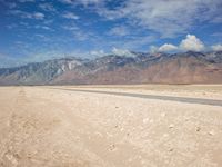 a desert field with a river in it with mountains behind it and clouds in the sky