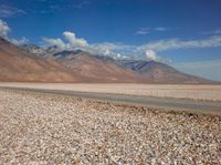 an open field with rocks in the foreground and mountain range behind it with some clouds