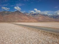 an open field with rocks in the foreground and mountain range behind it with some clouds