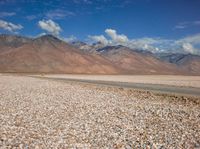 an open field with rocks in the foreground and mountain range behind it with some clouds