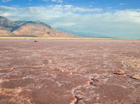 a very red desert plain with a hill in the distance to it and a person standing by on it