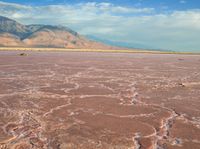 a very red desert plain with a hill in the distance to it and a person standing by on it