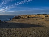 an empty beach with a small rocky area near the water and clouds in the sky