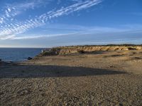 an empty beach with a small rocky area near the water and clouds in the sky