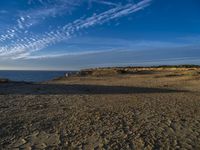 an empty beach with a small rocky area near the water and clouds in the sky