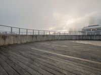 a wood floor on the boardwalk has fog coming out of it at night time and some buildings in the back