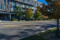 a tall black building near a roadway and a sidewalk in a city in autumn with lots of trees