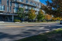 a tall black building near a roadway and a sidewalk in a city in autumn with lots of trees