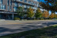 a tall black building near a roadway and a sidewalk in a city in autumn with lots of trees