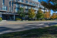 a tall black building near a roadway and a sidewalk in a city in autumn with lots of trees