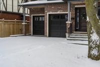 a house with snow all around and brick walls, black doors and a covered porch