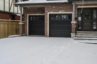 a house with snow all around and brick walls, black doors and a covered porch