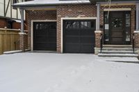 a house with snow all around and brick walls, black doors and a covered porch