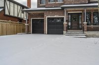 a house with snow all around and brick walls, black doors and a covered porch