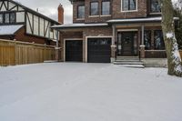 a house with snow all around and brick walls, black doors and a covered porch