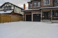 a house with snow all around and brick walls, black doors and a covered porch