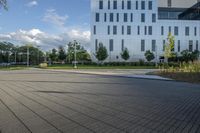 a city street surrounded by grass and tall buildings at the end of a street there is a paved pathway in front of the building