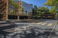 an empty intersection with a large building in the background with reflection of a leafy tree