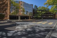 an empty intersection with a large building in the background with reflection of a leafy tree