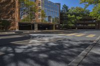 an empty intersection with a large building in the background with reflection of a leafy tree