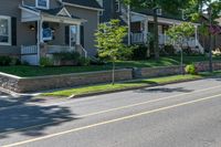 a man skateboarding along a residential street in a city, and there is also a brick wall on the side