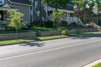 a man skateboarding along a residential street in a city, and there is also a brick wall on the side