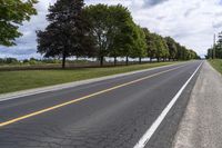 the empty roadway is lined with trees and grass in a countryside location on an overcast day