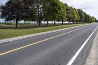 the empty roadway is lined with trees and grass in a countryside location on an overcast day