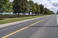 the empty roadway is lined with trees and grass in a countryside location on an overcast day