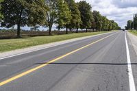 the empty roadway is lined with trees and grass in a countryside location on an overcast day