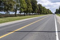 the empty roadway is lined with trees and grass in a countryside location on an overcast day