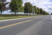 the empty roadway is lined with trees and grass in a countryside location on an overcast day