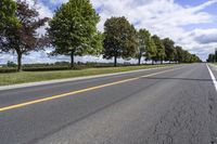 the empty roadway is lined with trees and grass in a countryside location on an overcast day