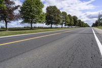 the empty roadway is lined with trees and grass in a countryside location on an overcast day