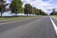 the empty roadway is lined with trees and grass in a countryside location on an overcast day