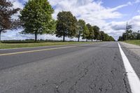 the empty roadway is lined with trees and grass in a countryside location on an overcast day