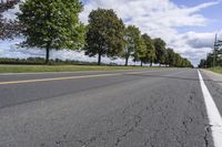 the empty roadway is lined with trees and grass in a countryside location on an overcast day