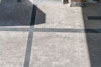 a woman on an outdoor bench looking down at the pavement in a courtyard area while a man holds his luggage