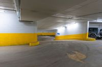 a car sits in an empty parking garage near yellow lines and yellow paint on the floors