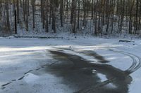 the road has two tires on the snow and a line of trees that is on top of a snowy hill