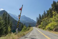 a road with the highway going through it is marked in black with a stop sign and mountains are behind