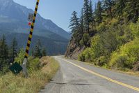 a road with the highway going through it is marked in black with a stop sign and mountains are behind