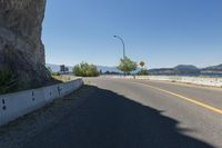 a scenic street lined with tall rocks with mountains and a lake in the background, viewed from near an overlook