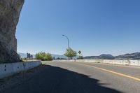 a scenic street lined with tall rocks with mountains and a lake in the background, viewed from near an overlook