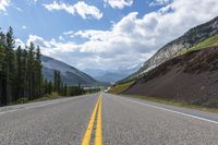 two yellow lines run on the empty highway through the mountains with pine trees on either side