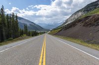 two yellow lines run on the empty highway through the mountains with pine trees on either side