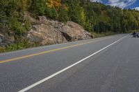 a motorcycle driving down a highway in the woods with trees and rocks on the hillside