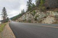 a motorcycle rides along a curved mountain road on a cloudy day, near the water